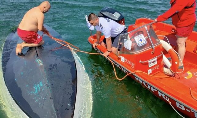 Wywrócona żaglówka na Wigrach Dwie osoby w wodzie bez założonych kamizelek i łódź odwrócona do góry dnem